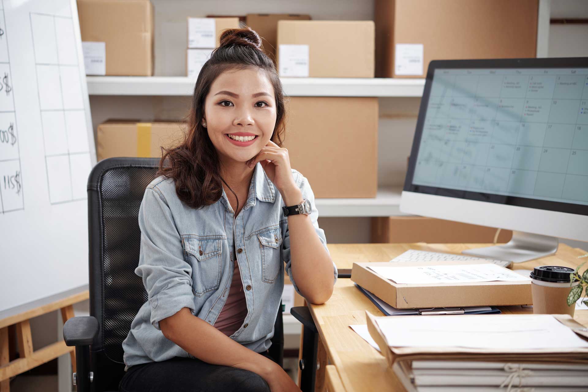 Woman sitting at a desk, smiling at the viewer, surrounded by papers and boxes